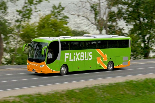 The green-orange Flixbus travels on the public road along a lake.