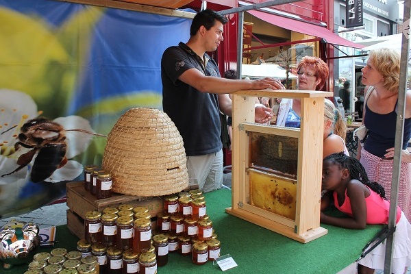 Marktstand auf dem Sjoemelmert in Roermond mit einem Imker, der den Besuchern etwas über Bienen, Honigtöpfe und einen Bienenstock erklärt.