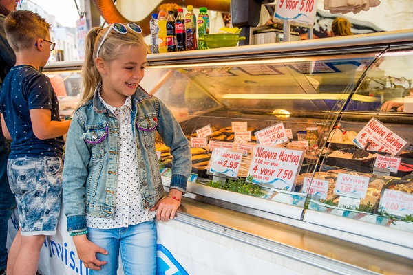 Meisje leunt tegen de counter van de visboer op de weekmarkt in Weert