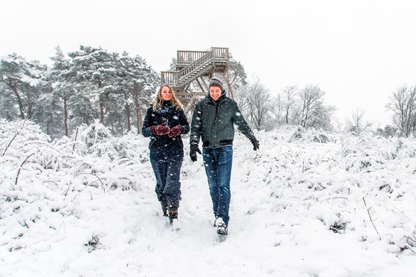 Twee wandelaars in de sneeuw bij een uitkijktoren op de Meinweg tijdens een winterwandeling.