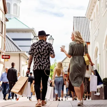 Bezoekers lopen samen door een winkelstraat bij Designer Outlet Roermond met shoppingtassen in de hand.