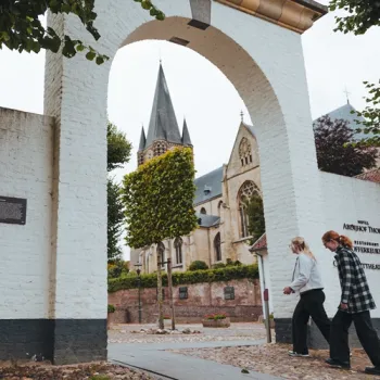 Poort naar de Abdijkerk van Thorn met twee wandelaars in het witte stadje.