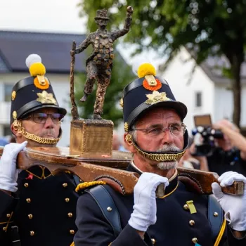 Schutters in traditioneel uniform dragen het bronzen beeldje d'n Um tijdens het Oud Limburgs Schuttersfeest.